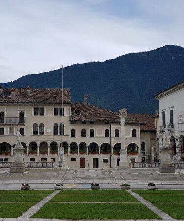 Piazza Maggiore a Feltre, con i palazzi, i portici, le fontane e le montagne sullo sfondo
