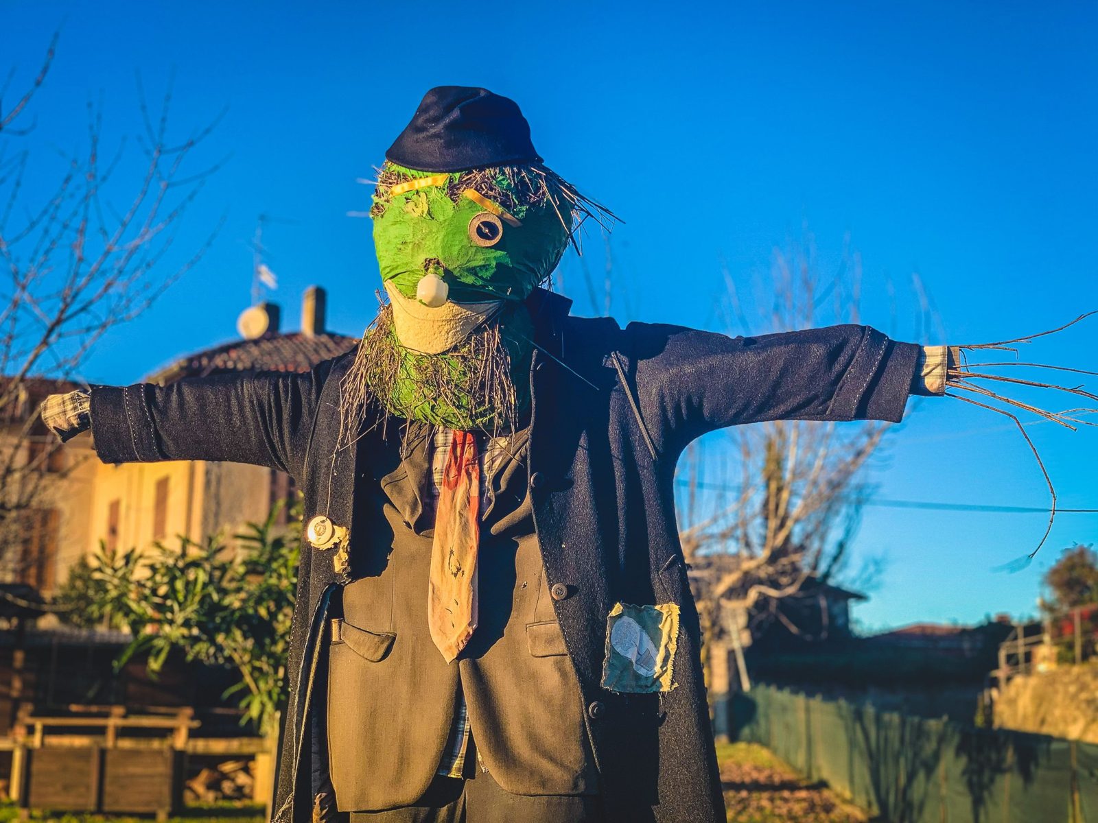 Spaventapasseri con la faccia verde, cappello e giacca, con le braccia aperte